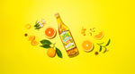 Angeleno Amaro bottle on bright yellow surface with ingredients spread around it.